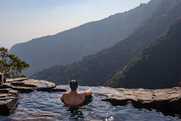 man enjoying the pristine view at natural swimming pool at mountain cliff from top angles