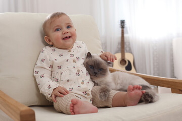 Cute little baby with adorable cat on armchair at home