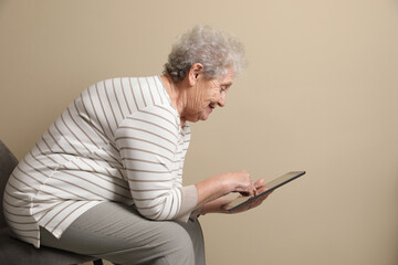 Elderly woman with poor posture using tablet on beige background - obrazy, fototapety, plakaty