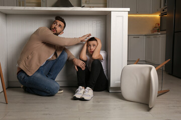Father and his son hiding under table in kitchen during earthquake