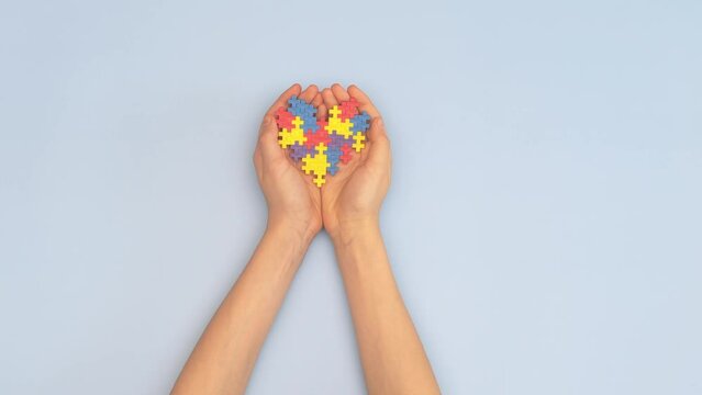 Child hands holding colorful puzzle heart on light blue background. View from above. World autism awareness day concept