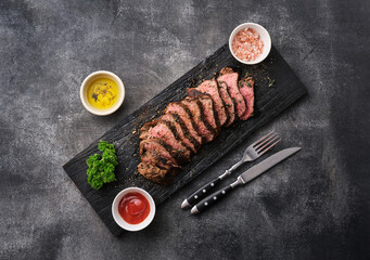 Grilled sliced beef steak on cutting board over grey table. Beef tenderloin steak. Filet Mignon recipe. - 495845919