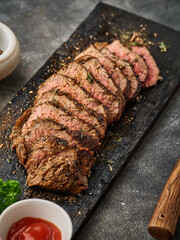 Grilled sliced beef steak on cutting board over grey table. Beef tenderloin steak. Filet Mignon recipe.