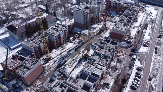 Aerial view of construction site in early spring with remaining snow. 4K drone footage with construction equipment, materials and unfinished buildings.