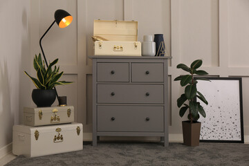 Obraz na płótnie Canvas Stylish room interior with storage trunks, grey chest of drawers and plants