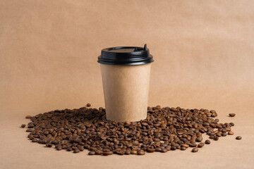 Takeaway brown paper coffee cup with black cap stands on roasted beans at brown background. Mock up