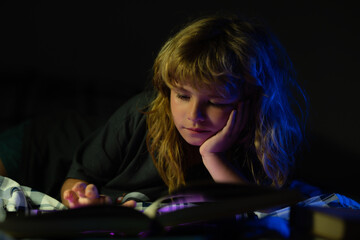 Child little boy reading a book in the dark home. Kids face with night light. Imagination or...
