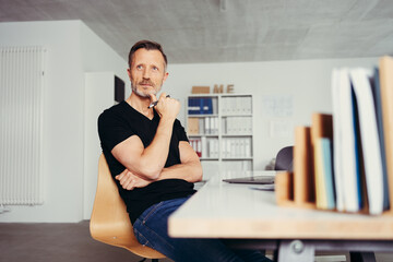 thoughtful man sitting at his desk in front of a laptop in his home office