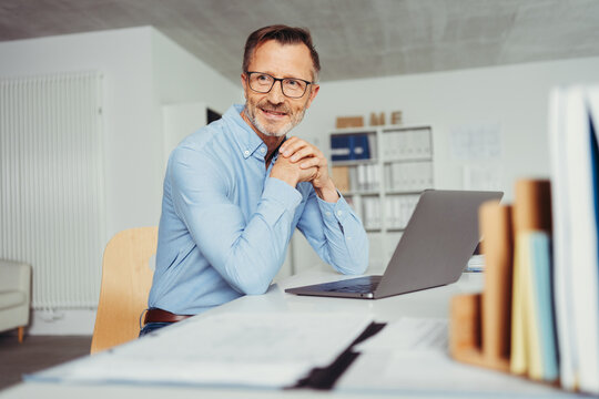smiling man sitting in home office at desk, in front of laptop