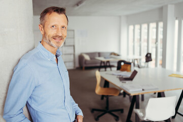 older businessman leans against a pillar in the office and looks into the camera