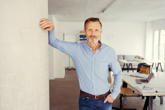 older businessman stands at a column in the office and looks into the camera