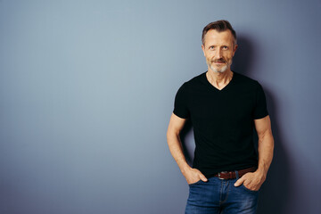 bestager with black shirt stands in front of a blue wall and looks into the camera