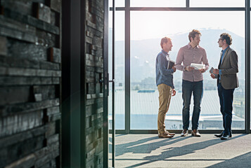 Getting organized before the presentation. Shot of male coworkers talking while standing in front of a window in an office.