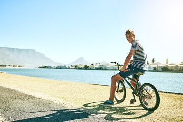 Fototapeta premium You wanna come for a ride. Full length portrait of a young boy riding his bike alongside a lagoon.