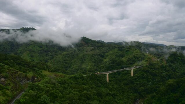 Aerial view of a bridge over the National Primary Route 27 and the Rio Grande de Tarcoles river, in cloudy Costa Rica - circling, drone shot