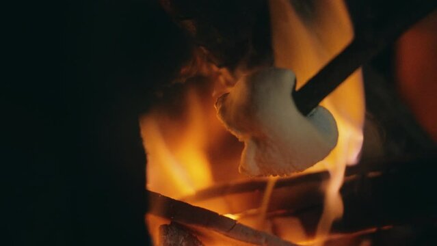 Close up of a Marshmallow getting roasted in a bonfire, nighttime - slow motion view