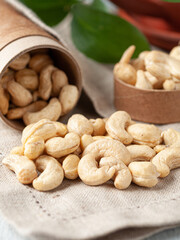 Peeled cashews are scattered on the table. There is a cardboard box next to it. Gray linen background. Close-up.