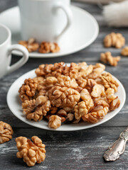 Peeled walnut in a white plate. Cups of tea nearby. Dark wooden background.