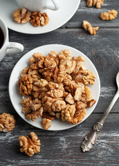 Peeled walnut in a white plate. Cups of tea nearby. Dark wooden background. View from above.
