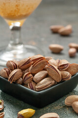 Pistachios in a black cup. In the background is a glass of beer. Dark background. Close-up. Macro.