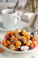 Assorted nuts, dried fruits and candied fruit. In a white plate. Close-up. Light background.
