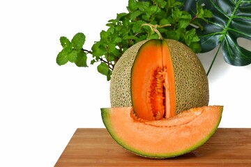Orange texture melon on a plank decorated with mint leaves monsterar leaves on a white background.