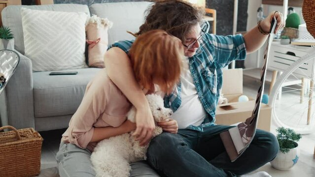 Couple in love sitting on the floor with their dog looking at a catalog with furniture materials in a new home