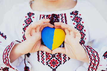 Small little girl in national traditional embroidery or embroidered shirt hold stone heart shape with Ukraine national flag. Love native country and people. Pray for Ukraine piece. High quality photo