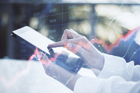 Close up of businessman hand using tablet with abstract red forex chart index on blurry outdoor background. Digital data, company and crisis concept. Double exposure.