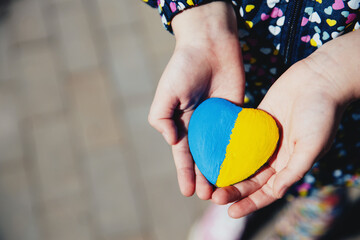 Small little kid hold heart shaped stone with Ukraine blue-yellow national flag or anthem. Girl...