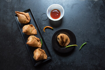Indian snacks samosa or triangle shaped fried food on a dark background made with flour, mashed potatoes, spices and peas. Top view. 