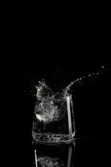 glass with water ice and splashes on a black background