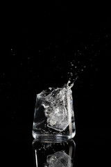 glass with water ice and splashes on a black background