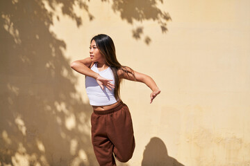 Woman dancing in front of warm beige wall with arms to side