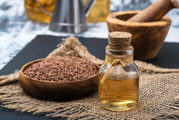 Glass bottle with linseed oil and flax seeds in a wooden bowl.