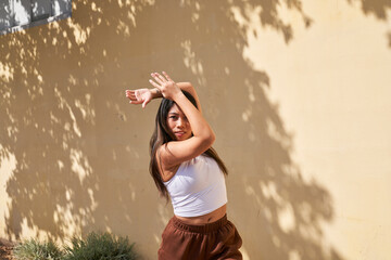 Woman dancing in front of warm beige wall with hand touching arm above head
