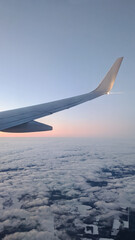 Obraz premium View from the window on the wing of an airplane with a light bulb on, blue sky, sunset and clouds. Place for text. Copy space. Vertical. Bird eye view. Airplane.