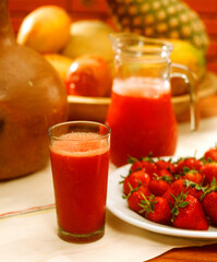 Fresh strawberry juice glass and jar on tropical fruits background.