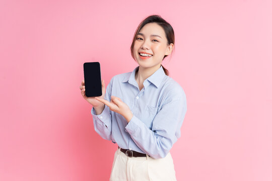 Image of young Asian girl holding smartphone on pink background