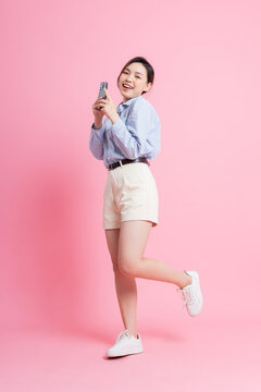 Full length image of young Asian girl using smartphone on pink background