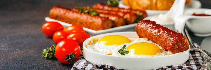 Breakfast - Fried eggs and meat sausages and sauces against a dark background. Selective focus. Copy space
