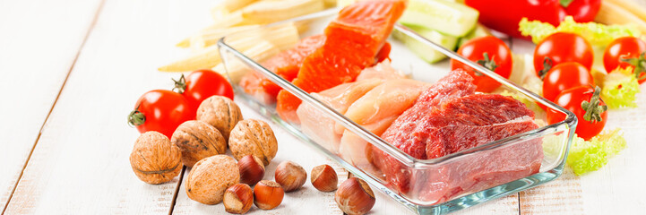 Products for a diet - raw meat of beef and chicken, a salmon and vegetables on a light wooden background. Selective focus.