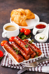 Meat sausages, croissant, coffee and sauces against a dark background. Selective focus.
