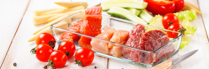 Products for a diet - raw meat of beef and chicken, a salmon and vegetables on a light wooden background. Selective focus.
