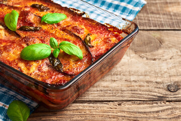Eggplant parmigiana on rustic wooden table. Italian traditional eggplant parmigiana pie with fresh basil and mozzarella cheese. Homemade eggplant parmigiana.