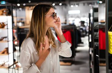Portrait of beautiful young woman choosing sunglasses in store. Shopping people fashion concept