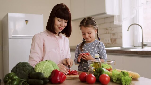 Caucasian young mom and cute small preschooler daughter have fun preparing food in kitchen together, caring mom teach little girl child cooking, help chop vegetables for salad, family weekend concep