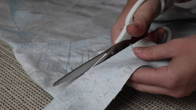 Closeup of young woman hands carefully cutting light blue fabric cloth material with white scissors