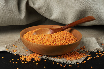 A bowl of red lentils on a rough napkin with a dark background.