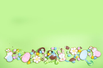 Happy Easter colorful flatlay. Colorful sugared and chocolate Easter eggs, sugar glazed cookies with festive holiday ribbon on light green background top view copy space